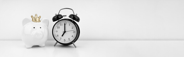 Black alarm clock with piggy bank against a white wall. Financial concept.