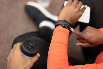 Young african american woman and man with bottle of water, checking pulse on fit tracker outdoor, cropped