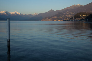 Como Lake.
Portion of Lake with snowy mountains, coast, a ferry, and little hamlet in the distance in sunset time.