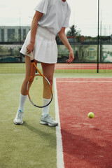 Sportive girl legs near the tennis racquet and balls. Cropped image of female legs on tennis court