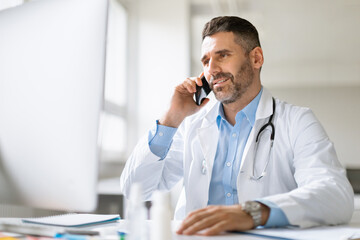 Cheerful professional male doctor having mobile conversation with sick patient, giving recommendations online