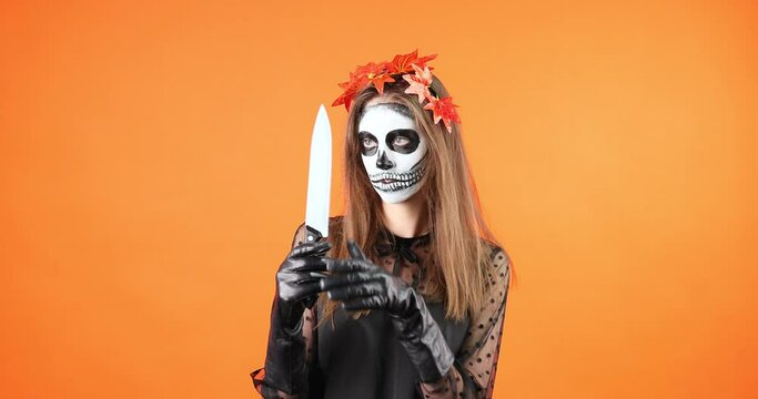 Fantasy portrait woman looking at camera, halloween makeup. Gothic girl holds dagger weapon in hands plays with edge knife.