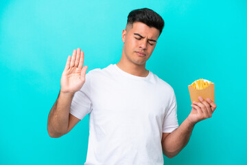 Young caucasian man catching french fries isolated on blue background making stop gesture and disappointed