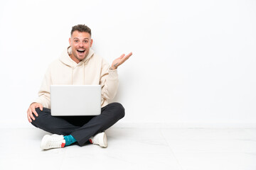 Young caucasian man with a laptop sitting on the floor isolated on white background with shocked facial expression