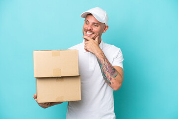 Delivery caucasian man isolated on blue background looking to the side and smiling