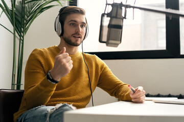 Man blogger smiling while broadcasting his live audio podcast in studio using headphones, laptop...