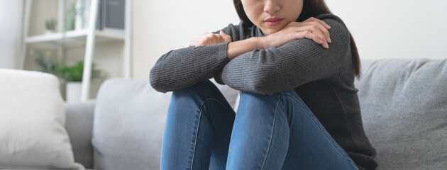 Unhappy anxiety young Asian woman covering her face with pillow on the cough in the living room at home. © Pormezz