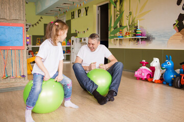 father and daughter have fun and play in the children's creative center, jump on a gymnastic ball