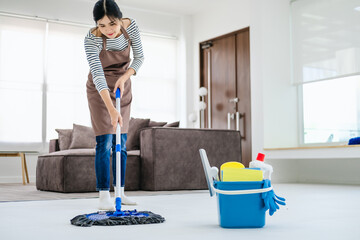 Asian woman mopping tile floor at living room while doing cleaning at home during Staying at home...