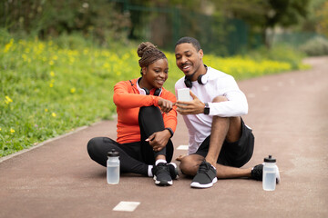 Happy young african american husband and wife sitting, talking with bottle of water, chatting in social networks