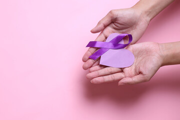 Purple ribbon and heart shape on palms hand isolated on pink background to support world epilepsy day and cancer awareness. 