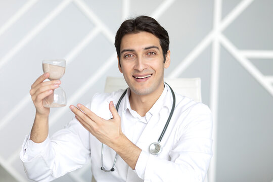 Close-up photo of smiling physician holding hourglass. Time and health concept
