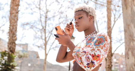 Focused black transgender person applying mascara on street