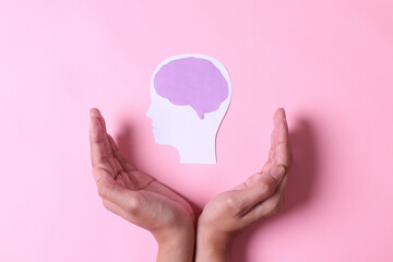 Hands with brain paper cutout isolated on pink background. World mental health day. 