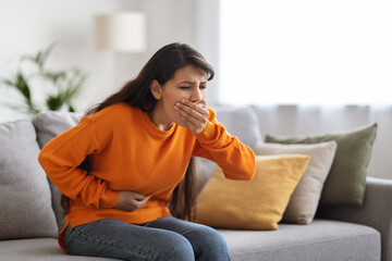 Sick middle eastern lady suffering from food poisoning, home interior