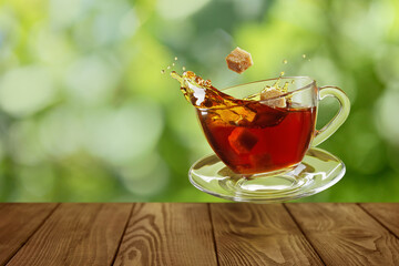 cup of tea with splash and falling brown sugar cubes on table