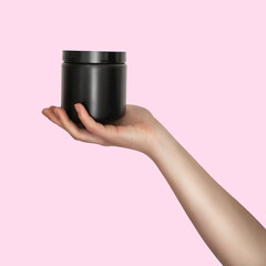 white woman hand holding a black plastic jar isolated on pink background