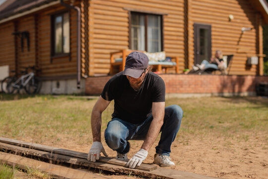 An adult man is engaged in carpentry work at a house construction site - a wooden fence and terrace boards