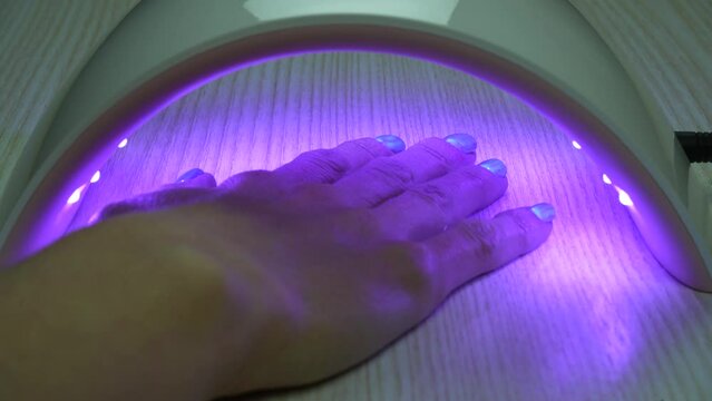 A hand with applied gel polish on the nail placed under the drying lamp, which automatically turning on
