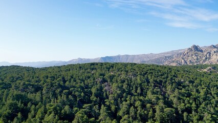 Aerial Majesty: Verdant Canopy of the Forest Meeting the Stoic Peaks of Aiguilles de Bavella,...