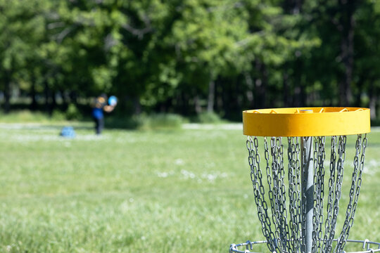 Disc golf player throwing a flying disc, chain basket target in the focus