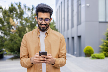 A young Hindu programmer engineer is walking outside an office building, a businessman is holding a phone and typing a message, a man in a shirt and glasses is smiling and browsing social media.