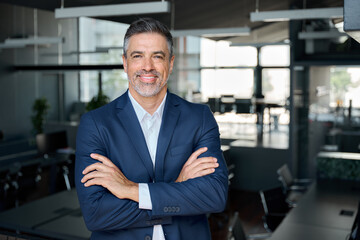 Happy middle aged business man ceo standing in office arms crossed. Smiling mature confident professional executive manager, proud lawyer, confident businessman leader wearing blue suit, portrait. - obrazy, fototapety, plakaty