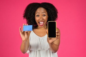 Happy surprised millennial african american curly lady show credit card and smartphone with blank space