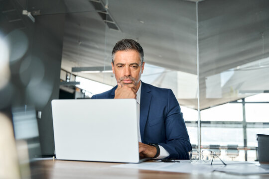 Concerned serious busy professional business man company ceo executive manager wearing suit looking at laptop computer sitting in office thinking of corporate management and financial strategy.