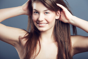 Beauty, face and smile portrait of a woman in studio with hands in hair care, makeup and cosmetics. Headshot of happy young female model on a grey background for natural glow, skincare or dermatology