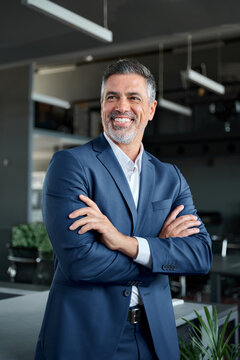 Happy confident middle aged business man, mature professional ceo corporate leader wearing blue suit standing in modern office with arms crossed looking away laughing, authentic vertical portrait.