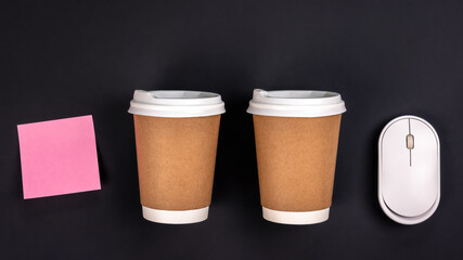 Paper cups, computer mouse and paper sticker on a dark background, top view.