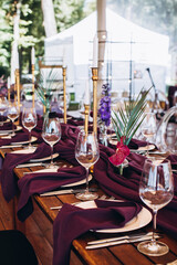 Wedding decor. Banquet. The tables are decorated with compositions of colorful flowers and greenery, violet tablecloths, candles, glasses, plates, and purple napkins.
