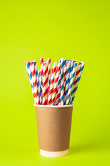 Disposable paper cup with striped paper straws on a green background.
