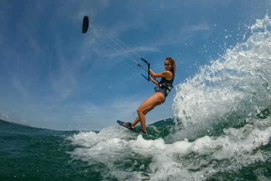 Kitesurfing girl in black sexy swimsuit with kite in sky on board in blue sea riding waves with water splash. Recreational activity, water sports, action, hobby and fun in summer time. Kiteboarding sp