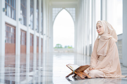 The image of an Asian Muslim woman in the Islamic religion in hijab in cream color. reading the Quran and having a happy smiling face Staying in a beautiful mosque out of respect for God.