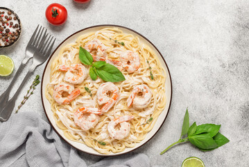 Spaghetti pasta with shrimp in a creamy sauce in a plate on a light stone background. Top view, flat lay, copy space. Mediterranean or Italian kitchen.