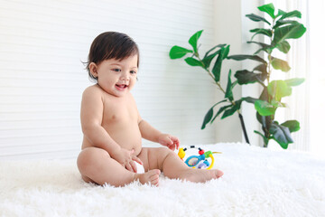 Portrait of smiling crawling baby sits on fluffy white rug, little cute kid girl playing with developmental toys, happy daughter child playing and laughing, love in family, childhood care and learning