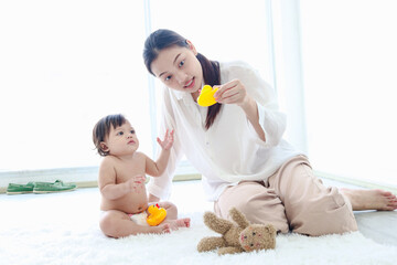 Fototapeta premium Happy toddle baby kid and mother sit on fluffy white rug floor in living room, little girl daughter and mom play with toys together, parent take care, look after infant child at home, love in family.