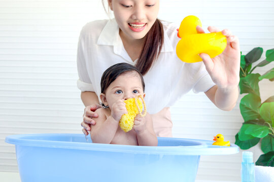 Happy Toddle Baby Infant Has Fun While Take Bath In Bathroom, Mother Hold Yellow Duck Toy During Bathing Kid In Tub, Mom Washing And Cleaning Toddler Girl Daughter Child In Bath, Childhood Parent Care