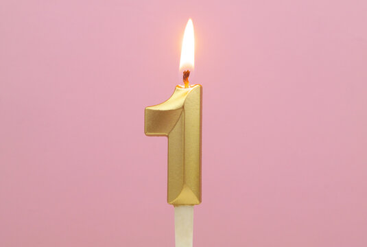 Golden birthday candle burning on pink background, number 1.