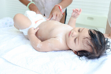 Happy toddle baby infant child lying on white towel after bathing and mom applying powder on body,...