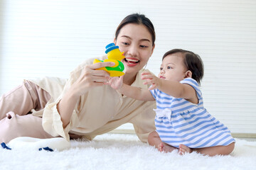 Happy toddle baby kid and mother sit on fluffy white rug floor in living room, little girl daughter and mom play with toys together, parent take care, look after infant child at home, love in family.