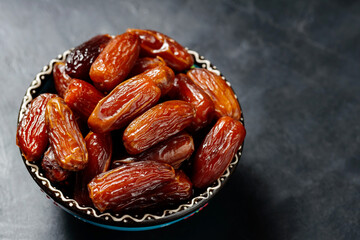 Dried dates in bowl on a dark background. Healthy organic vegetarian food. Top view. Copy space