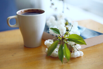 A branch of white sakura on the table next to a white cup of coffee.