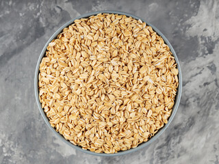 Dry oat flakes in bowl on a gray background. Oat groats flattened into flakes. Top view. Copy space