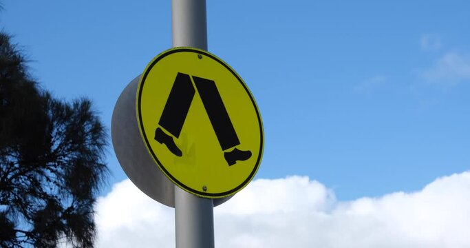Close up of pedestrian crossing signs on metal pole in strong wind. The sign features yellow background with a black walking symbol that complies with Australian Standards.  Melbourne VIC Australia