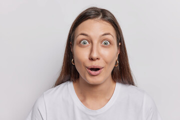 Scared terrified brunette young woman shocked with prices at shop keeps jaw dropped dressed in casual t shirt stands against white background reacts to something amazing. Human reactions concept