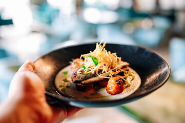 man hand hold Fried fillet fish with tomatoes and sauce on plate