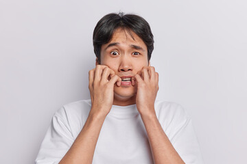 Scared anxious man stares with terror at camera keeps hands near mouth dressed in casual t shirt...